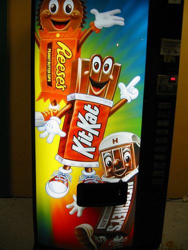 A photograph of a candy vending machine that has characterized happy candy cartoon figures on it.