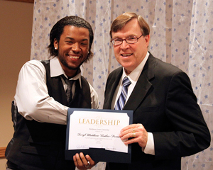 A photo of a student shaking hands with a teacher while being awarded a leadership certificate