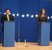 A photograph of a man and a woman during a political debate. Each is standing behind a podium.