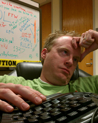 A photograph of a man sitting at his desk. He looks like he is sick.