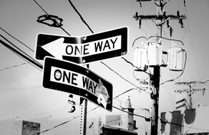 A photograph of two 'one way' signs. One points left and the other points right.