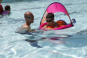 A photograph of a swim coach teaching a little boy how to swim using a flotation device.