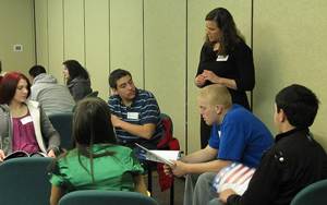 A photograph of a group of students at a conference sitting in a circle looking at various printed literature and having a discussion.