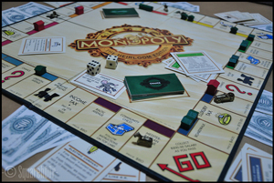 A photograph of the board game Monopoly. It shows the game board, the cards, the game money, and a pair of dice.