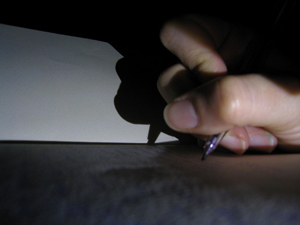 A photograph of a person's hand writing with a pen on a piece of paper. 