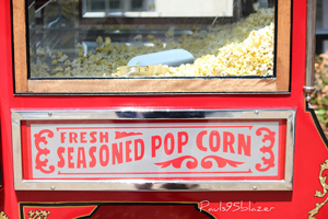 A photograph of a large popcorn popper. It has a sign that reads “Fresh Seasoned Popcorn”