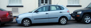 A photograph of a car parallel parked between two other cars