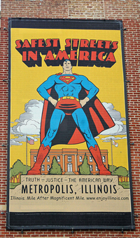 A Superman poster on the outside of a building. The poster reads: ‘Safest Streets in America: Truth-Justice-The American Way: Metropolis Illinois.’ Superman is standing in the foreground.