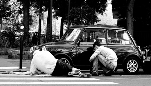A photograph of a father and son talking while working on a car.