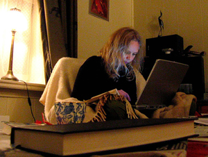 A photograph of a young woman sitting on a chair and looking at a laptop screen.