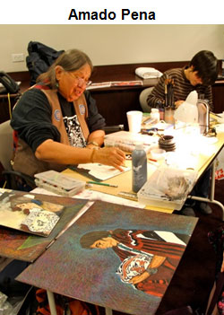 image of Amado Pena, seated at a table with several paintings in front of him. A student sits at the table with him