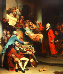 A man in a red coat and white wig standing on a platform with his right hand raised addressing a group of seated men in colonial dress.