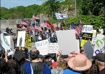 Two groups of people. One of them are holding signs against the Iraq War. The others are largely holding American flags supporting the war