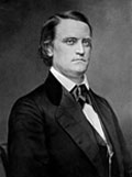 Portrait of a man with parted hair wearing a dark suit, white dress shirt and a closely tied string tie