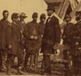A group of men in military uniforms standing outside of a tent around a tall man in a black suit and stovepipe hat.