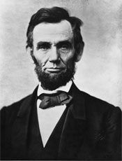 A head and shoulders photograph of a man with a black beard, in a suit and a bow tie.