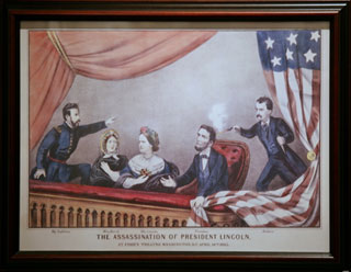 A color image of a man firing a gun into the back of the head of a bearded man in a theater balcony.