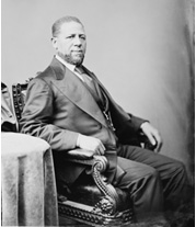 An African American with in a three piece suit seated in an ornate chair.