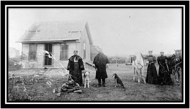An African American family and their two dogs standing in front of a home on a dusty front porch area.