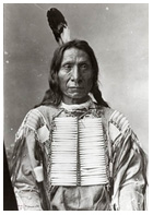 A man in an American Indian shirt with a single feather headdress and long hair.