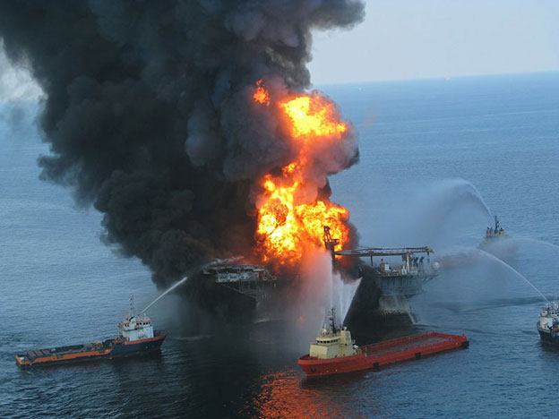 Image of the Deepwater oil rig burning in the Gulf of Mexico, surrounded by boats that are spraying the fire with water. 