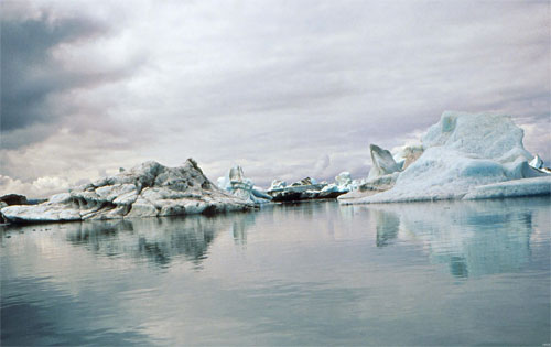 Photo of five blocks of ice in the form of small mountains sitting on the lake.