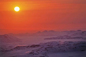 Image of a tundra landscape of a mountain range covered in snow with a sunrise.