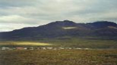 Image of a grassy field covered partially in snow with large mountains in the background