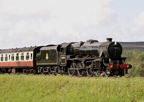 This is a photo of a black  steam locomotive riding through the countryside