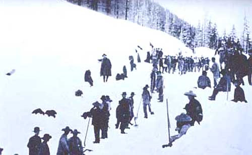 Image of many men standing on a snow covered mountain. Many of the men are wearing straw, wide brimmed hats, typical of the Chinese.