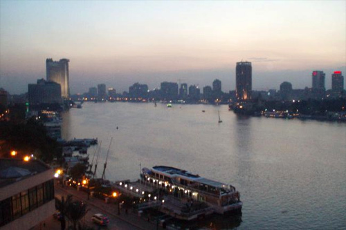 Image of The Nile River in Cairo at dusk. A boat at the dock can be seen in the foreground and different buildings line the shores of the river on both sides.