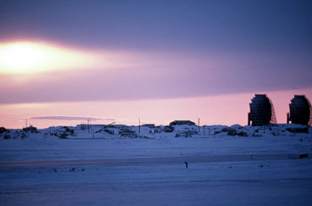 Image of a snow covered area with a set of structures in the background and visible antennae.