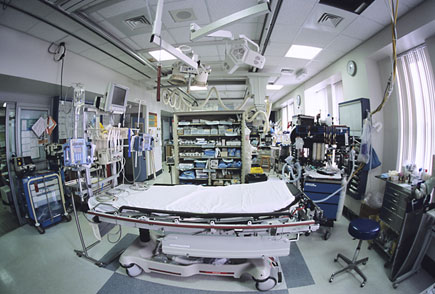 Image of an emergency room with a hospital bed surrounded by various pieces of emergency equipment.