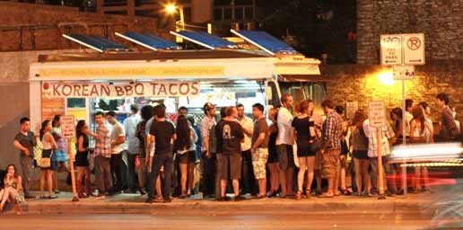 Image of  several people waiting outside of a food truck with a large sign that reads, “Korean BBQ Tacos