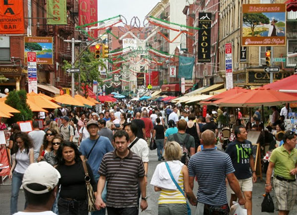 Image of modern-day Mulberry Street. The street is crowded with people walking. The street and sidewalks are lined with shops and vendors. 