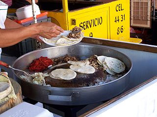 Image of a person assembling a taco made of flour tortillas, grilled meat, beans and onions.