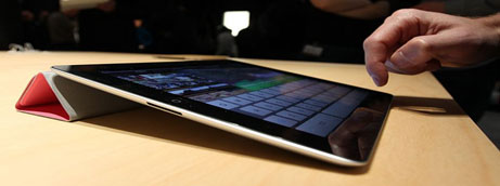 Image of an iPad 2 leaned against a smart cover; a finger is poised to touch the virtual keyboard that is displayed.