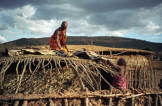 Image of two women repairing a hut with straw and sticks