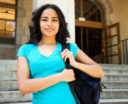 Image of a female student wearing a backpack, standing in front of a college building