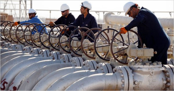 Image of four men wearing hardhats and dressed in field suits turning the wheels at respective oil pumps