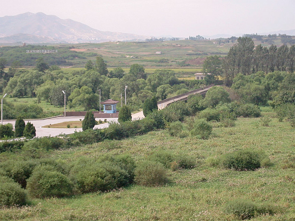 Image of the Bridge of No Return, heading into North Korea. There are rolling hills in the foreground and mountains in the background.