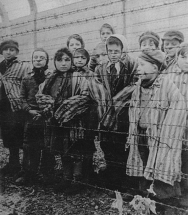 Image of children standing behind barbed wire. They are clothed in striped uniforms.