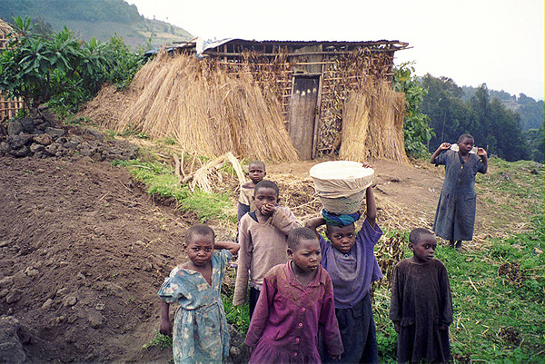 Image of several young children standing in front of a hut covered in straw.