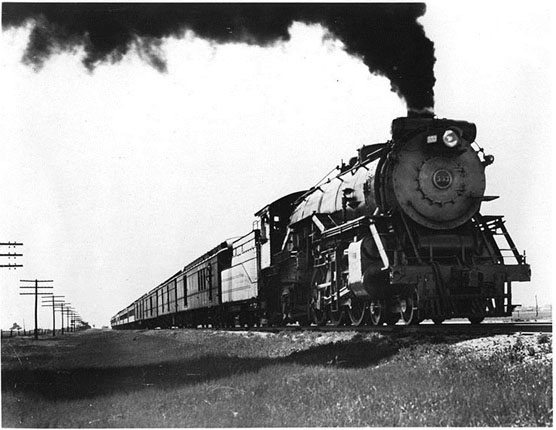 A 1929 photograph of a moving steam locomotive belching smoke.