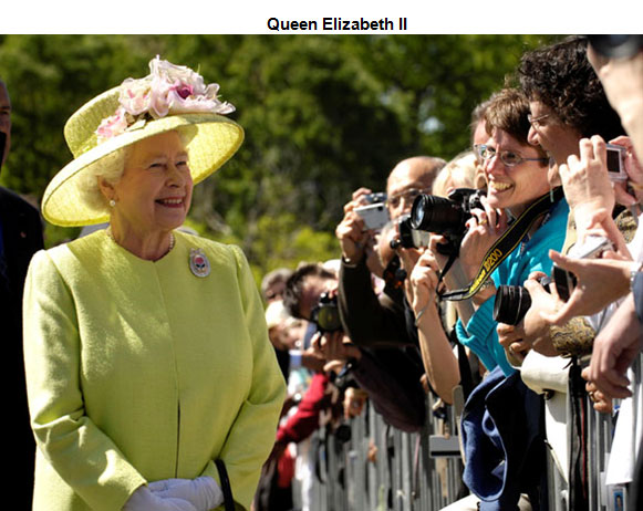 Image of Queen Elizabeth II standing in front of spectators who are behind a security barrier. 