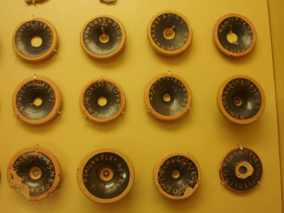 A photograph of Greek voting tokens; round clay disks with Greek writing/names inscribed on them.