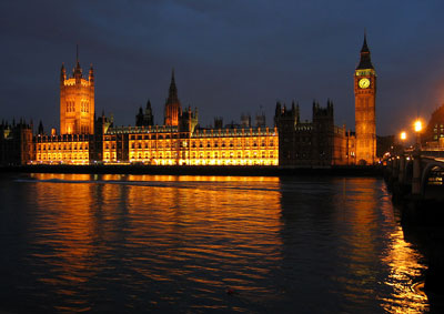 A nighttime view of the Palace of Westminster at night from the river Thames. It is a large gothic looking building with several pointed spires lit up to standout against the night sky.