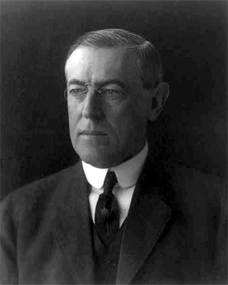 photograph portrait of President Herbert Hoover. He is a late middle aged man wearing glasses. He is wearing a suit, vest and tie.
