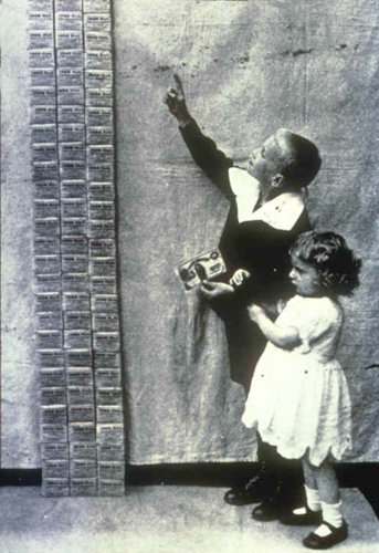 A photograph of a boy and girl looking at tall stacks of German Marks (paper money). The stacks are much taller than they are.