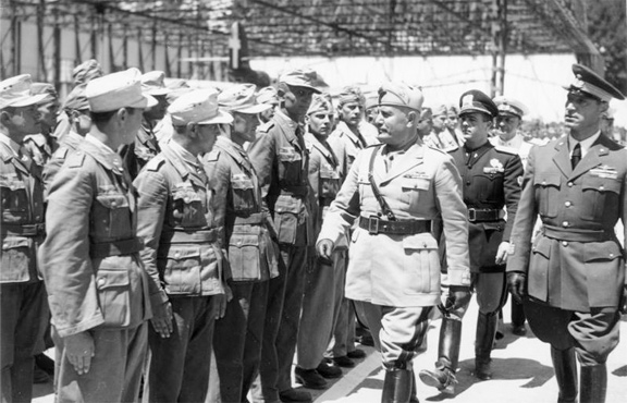 A photograph of Benito Mussolini in uniform reviewing troops in formation.